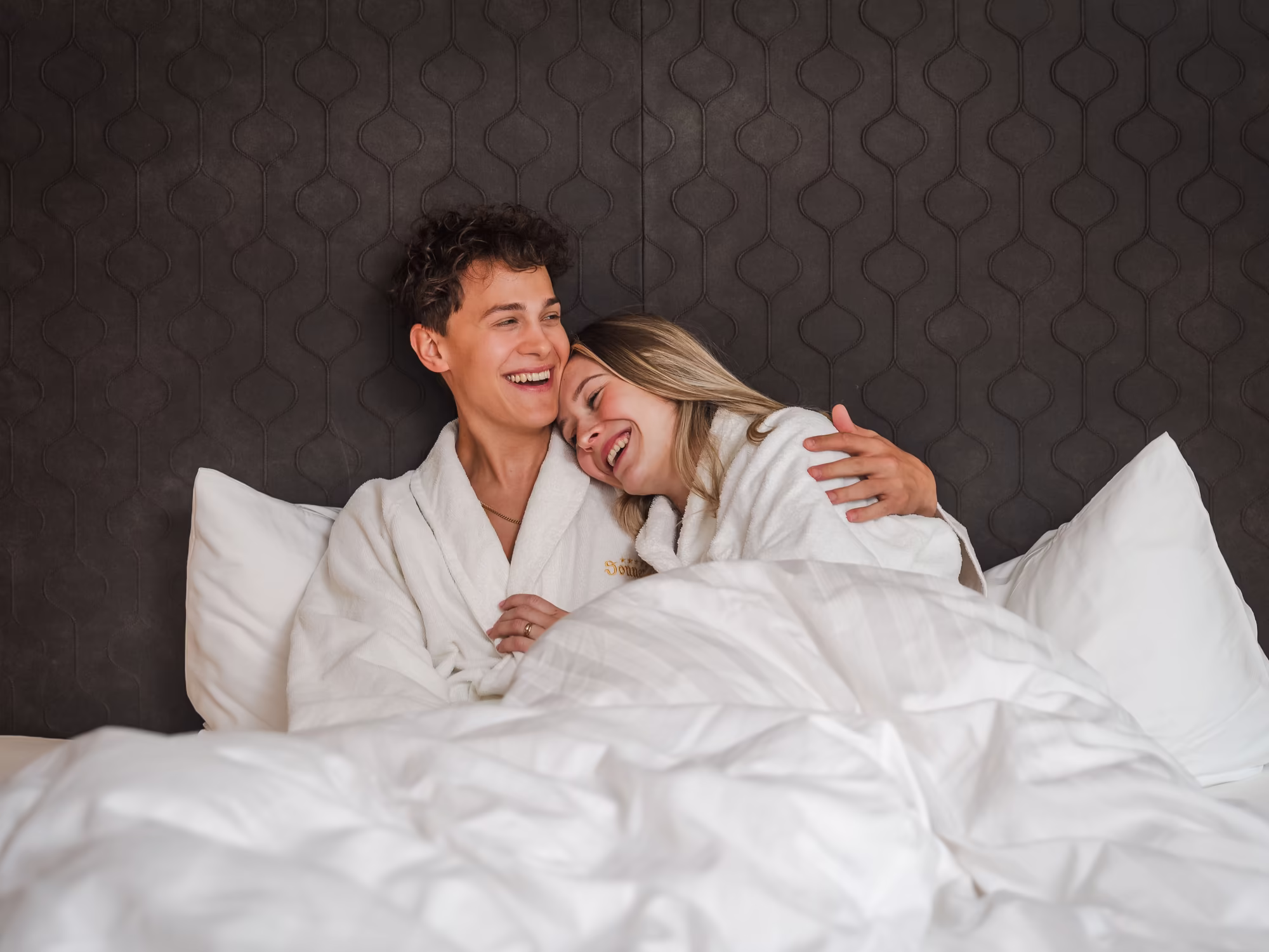Junges Paar in Bademänteln im Bett, lachend
