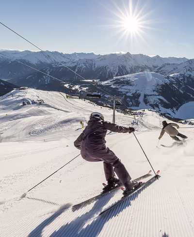 Skifahrer bei der Abfahrt auf einer sonnenbeschienenen Piste