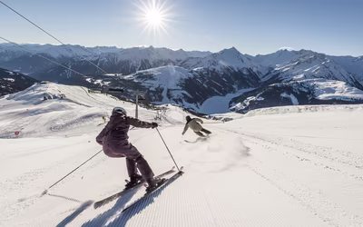 Skifahrer bei der Abfahrt auf einer sonnenbeschienenen Piste