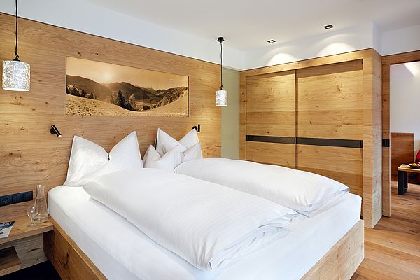 Blick auf das Doppelbett mit moderner Holzvertäfelung und hinterleuchtetem Bild sowie Kleiderschrank in der Superior Suite des Landhauses