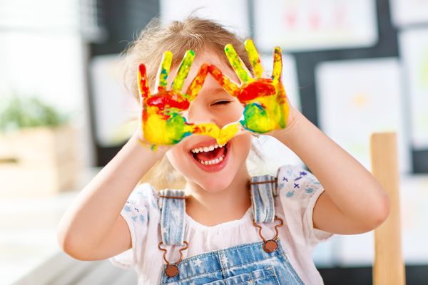 Lachendes Mädchen mit Fingerfarben an den Händen, die sie vors Gesicht hält © jenkoAtaman