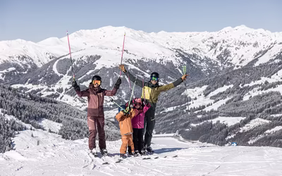Familie posiert mit Skistöcken in der Luft für ein Foto